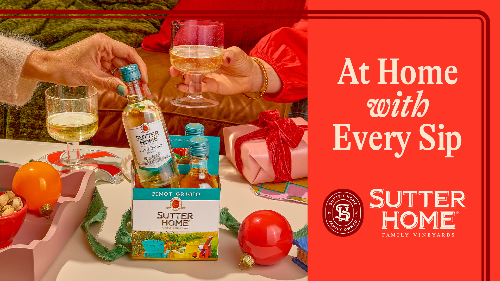 Sutter Home festive table with gifts, ornaments, mini bottles, and filled wine glass on table, with hand holding filled wine glass, and sidebar with red background and text foreground 'At Home with Every Sip' with Sutter Home logo